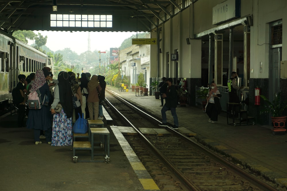 Un grupo de personas de pie junto a un tren en una estación de tren