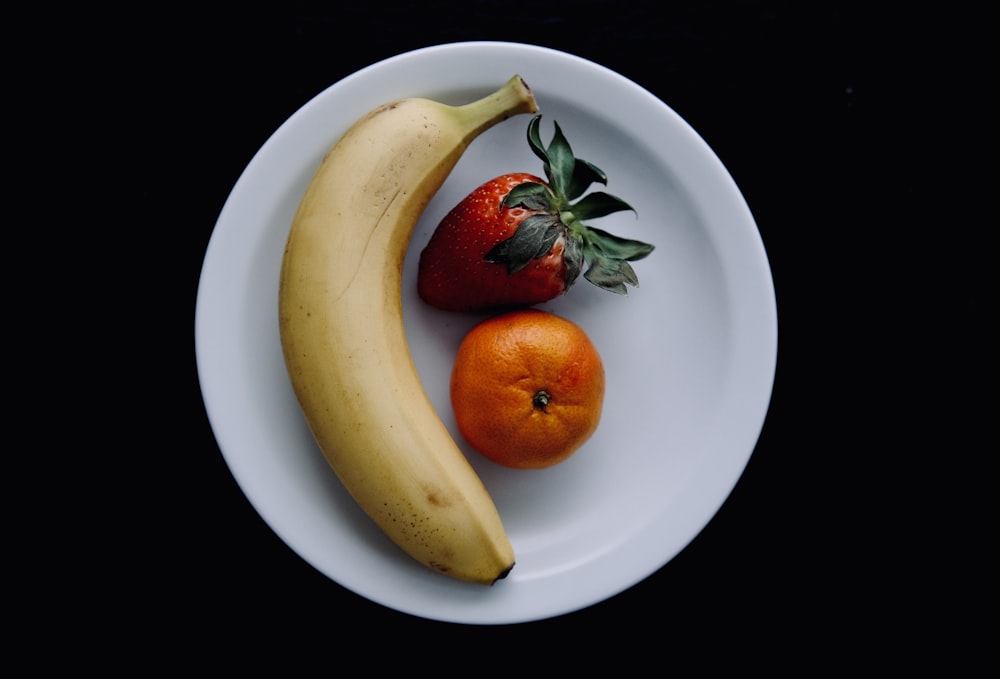 a banana, orange and strawberry on a white plate