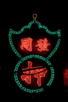 Bright neon sign with Chinese characters illuminated in red, outlined by green decorative patterns against a dark background.