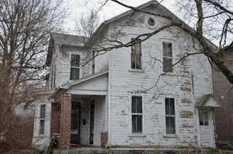 A worn-down house with peeling paint where three children stand outside, looking hopeful.