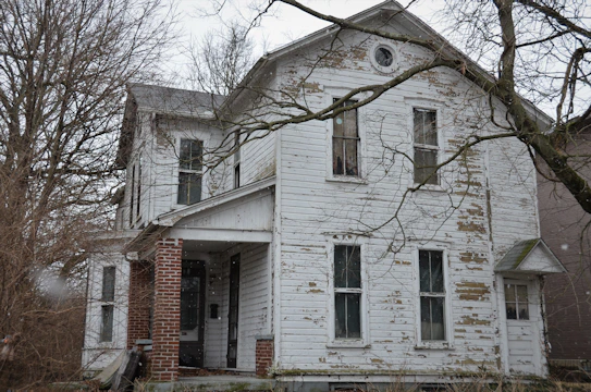 A worn-down house with peeling paint where three children stand outside, looking hopeful.