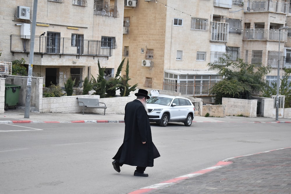 a man walking across a street next to a white car