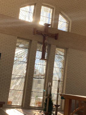 A warm, inviting church interior with sunlight streaming through stained glass windows, highlighting a cross at the altar.