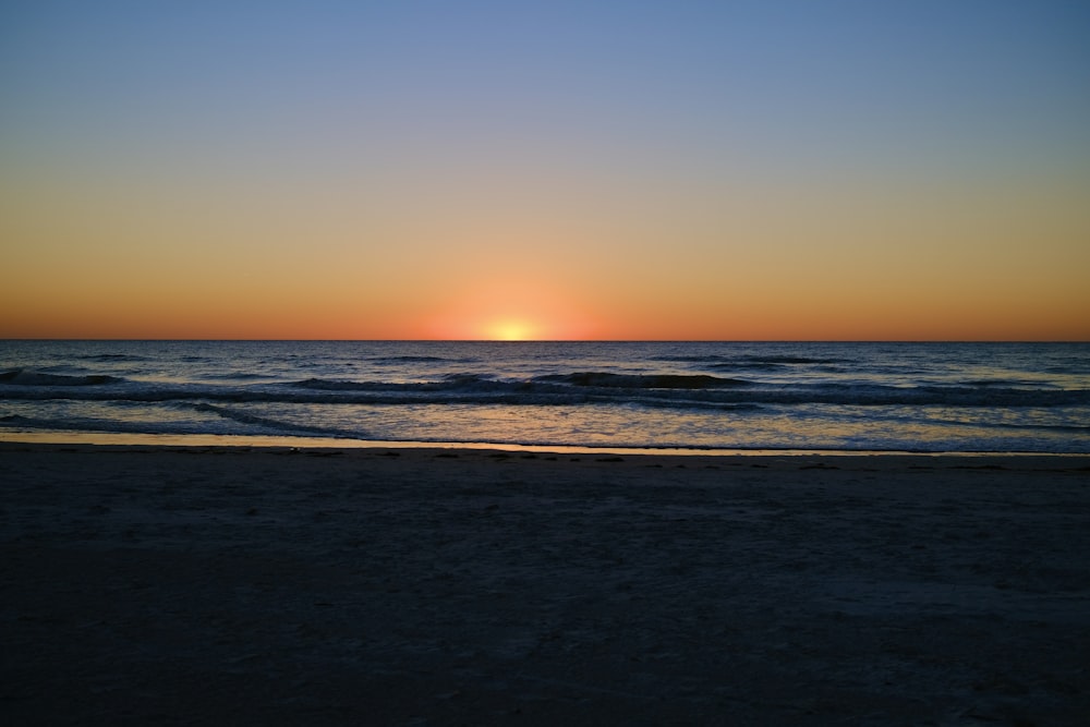 the sun is setting over the ocean on the beach