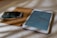 A close-up view of a digital tablet placed on a light brown surface. Next to it, a dark leather wallet containing several credit cards is visible. The tablet displays a chart with various colored bars against a light-colored background, suggesting a data analysis or report.