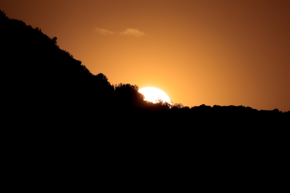 the sun is setting over a hill with trees