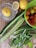 A variety of fresh vegetables and fruits are arranged on a wooden surface. There is a lemon in a glass juicer, a whole lemon, a sliced half lemon, several cucumbers, spring onions, mint leaves, and a green plastic basket containing assorted cherry tomatoes of different colors.