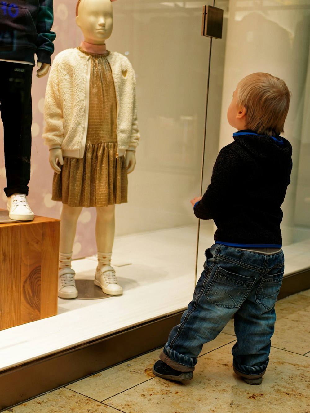 a little boy standing in front of a mannequin