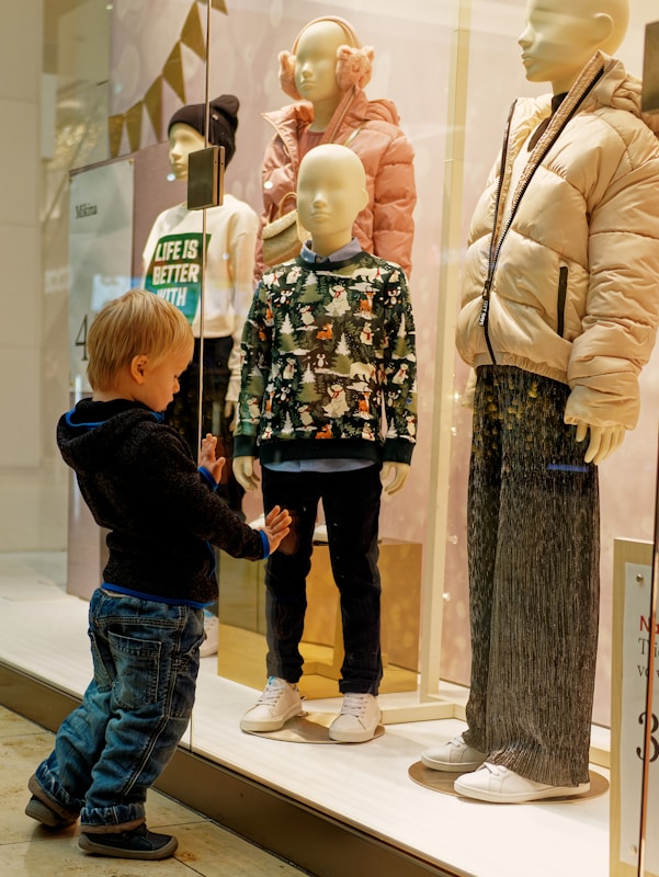 a little boy standing in front of a display of mannequins