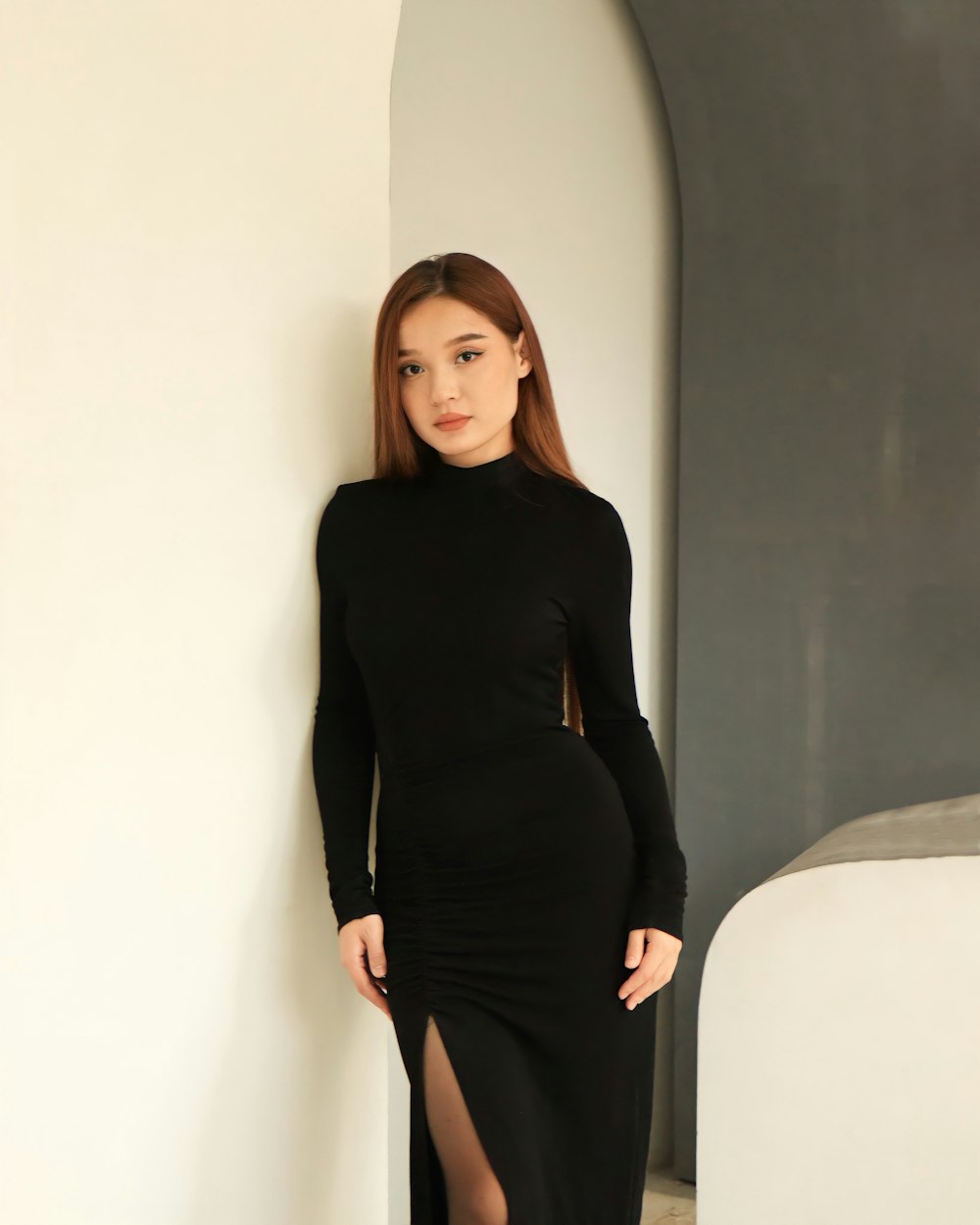 a woman in a black dress leaning against a wall