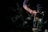 A person is holding a collection of climbing gear, specifically carabiners and other climbing equipment, against a dark background. The scene appears to be in low light, focusing on the hand and gear.