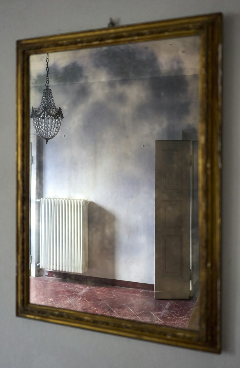 a mirror reflecting a room with a radiator and a chandelier