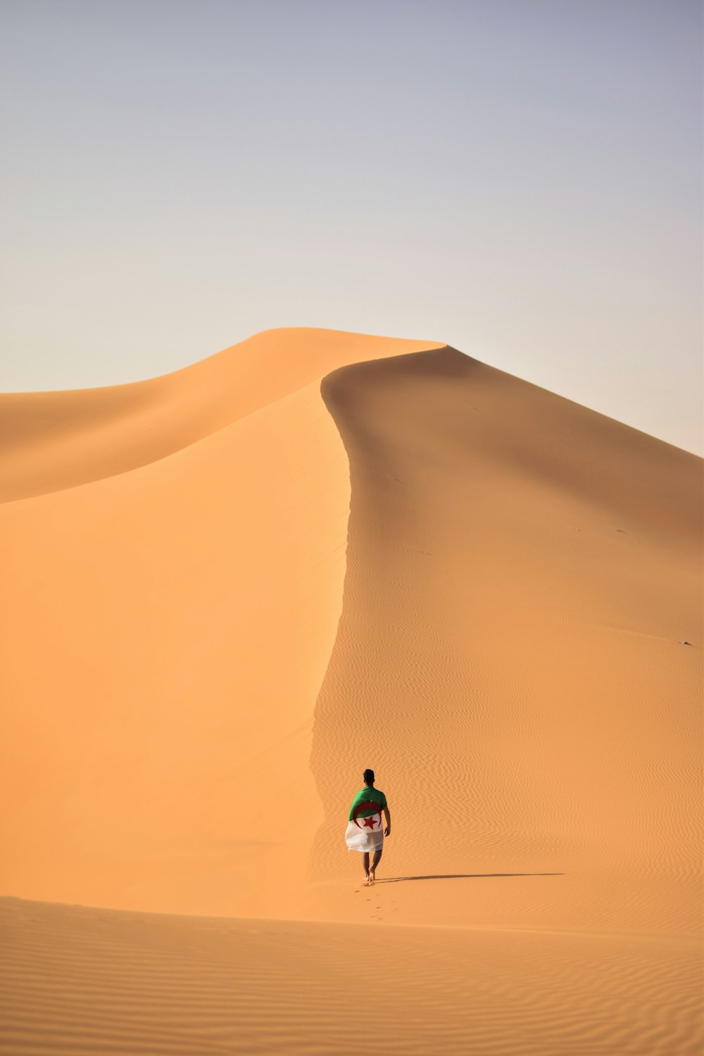 a man walking across a sandy desert with a surfboard