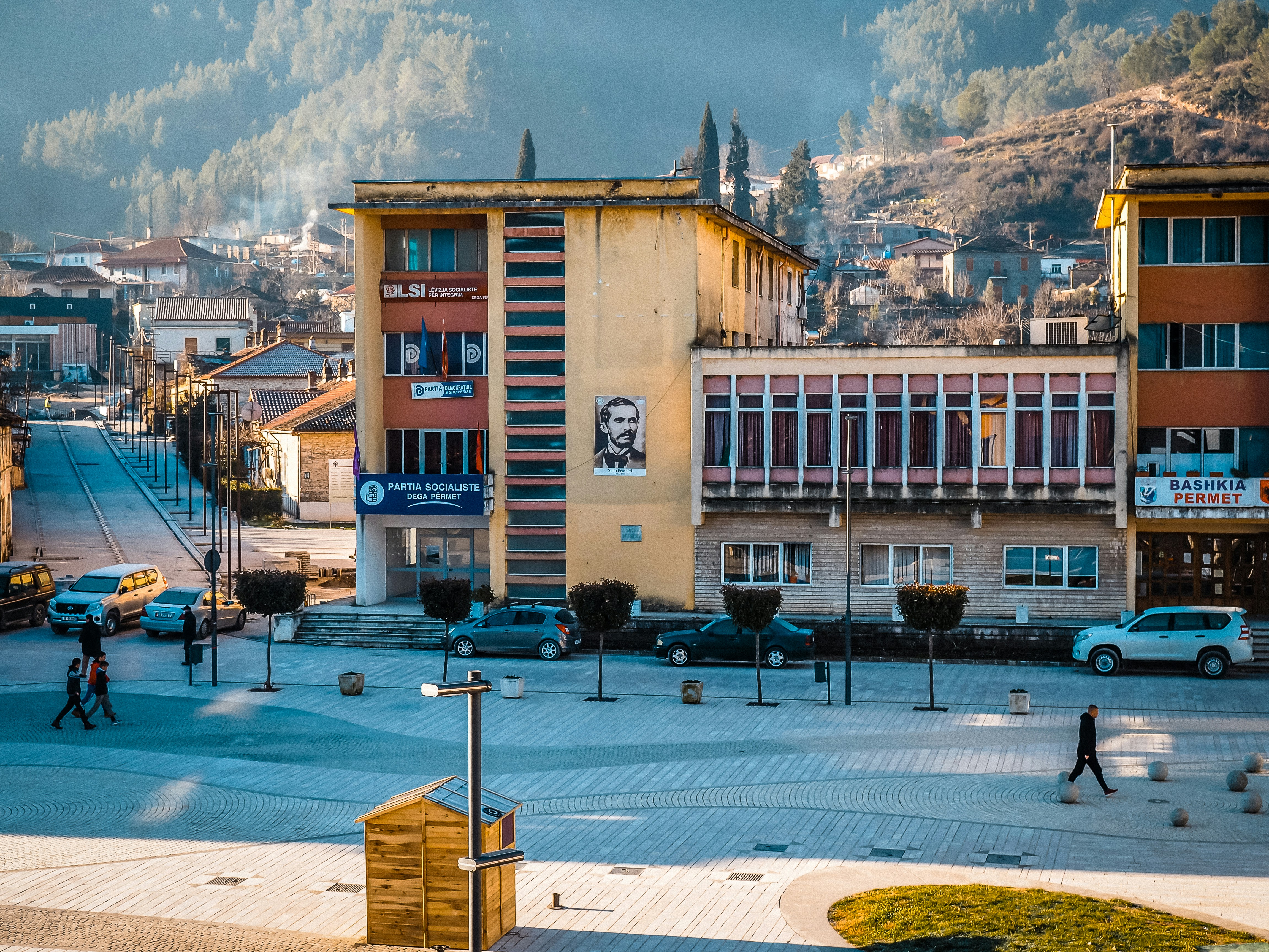a town square with cars and people walking around