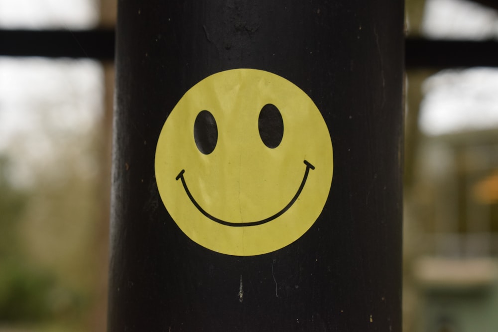 a yellow smiley face sticker on a black pole