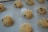 Several scoops of chocolate chip cookie dough are placed evenly on a sheet of baking parchment, ready to be baked.