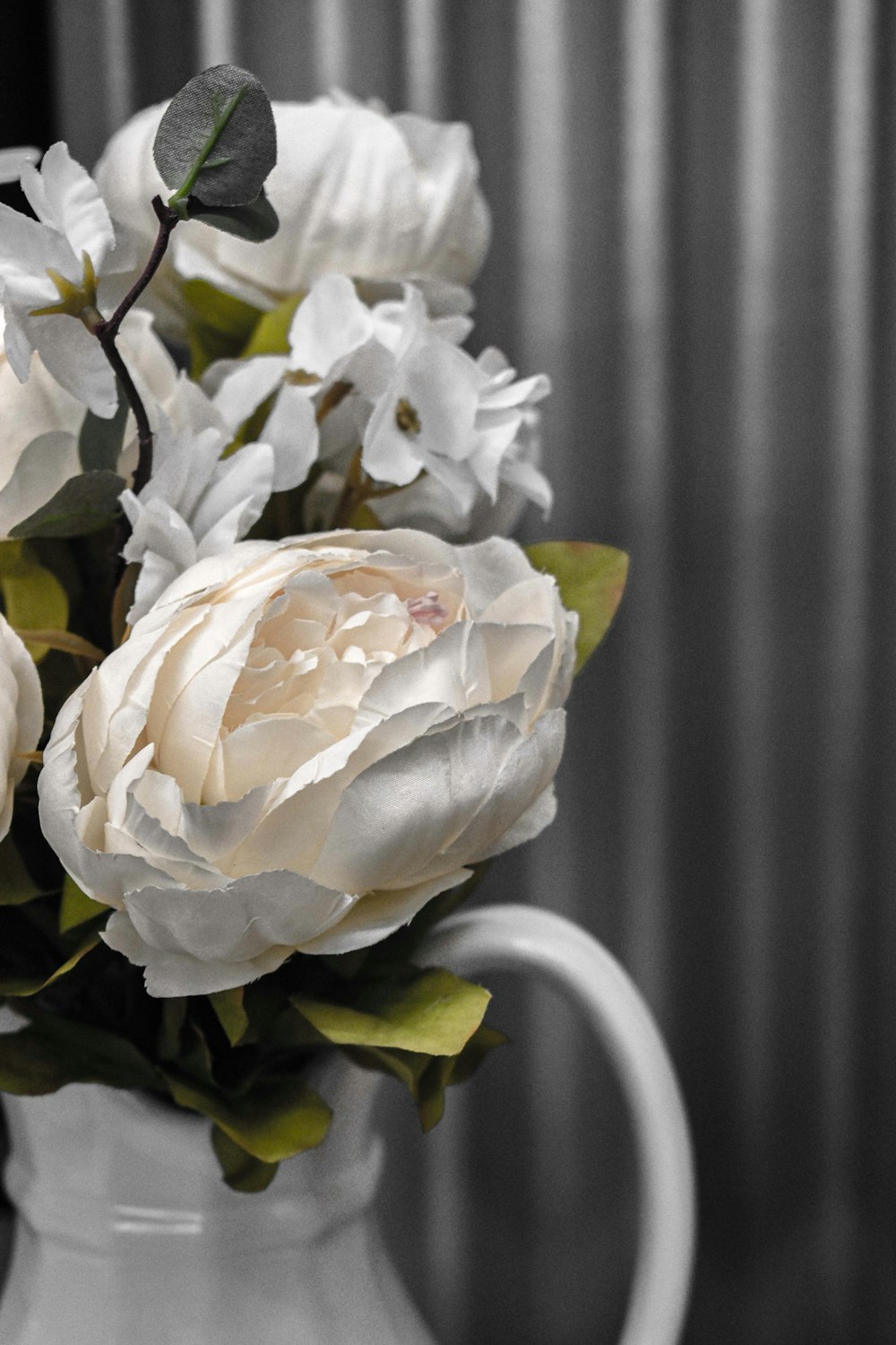 um vaso branco cheio de flores brancas em cima de uma mesa