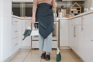 A friendly cleaner organizing cleaning supplies in a bright, tidy home kitchen.
