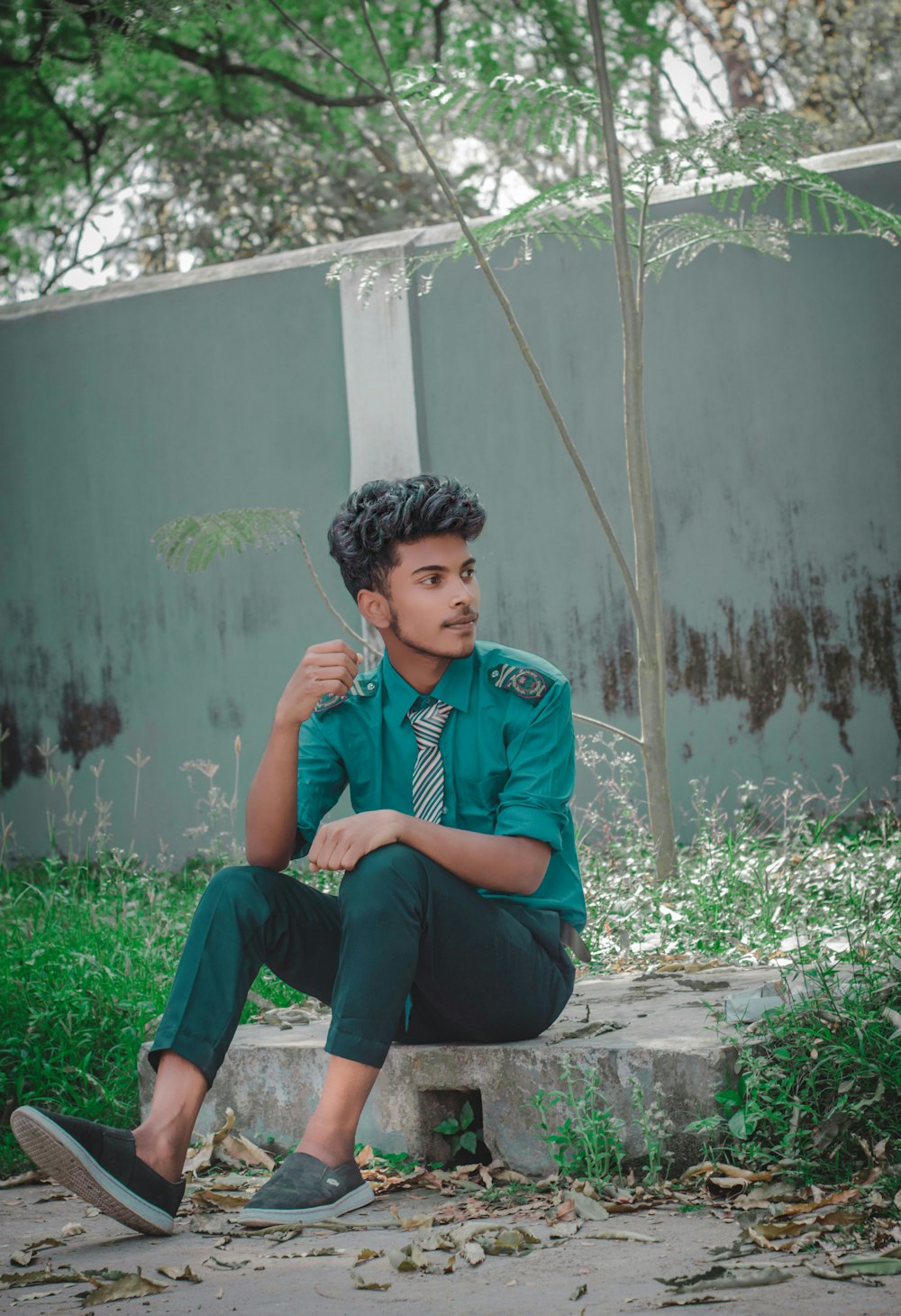 a boy in a green shirt and tie sitting on a concrete step