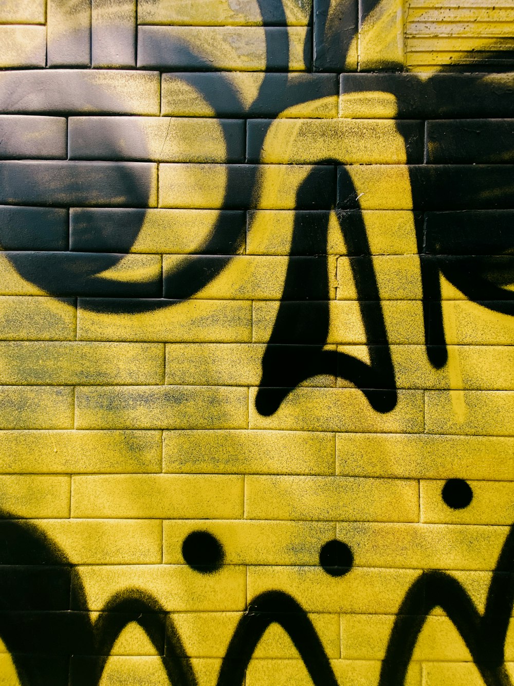 a yellow brick wall with black graffiti on it