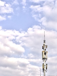 A telecommunications tower stands against a backdrop of a partly cloudy sky. The structure is equipped with various antennas and equipment, suggesting its use for communication purposes.