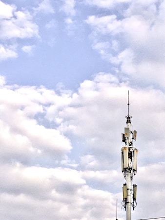 A telecommunications tower stands against a backdrop of a partly cloudy sky. The structure is equipped with various antennas and equipment, suggesting its use for communication purposes.