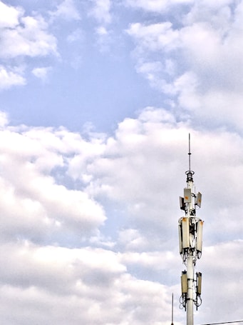A telecommunications tower stands against a backdrop of a partly cloudy sky. The structure is equipped with various antennas and equipment, suggesting its use for communication purposes.