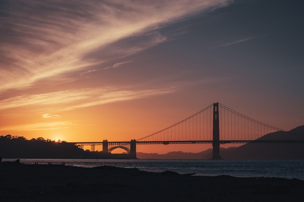 the sun is setting over a bridge over a body of water