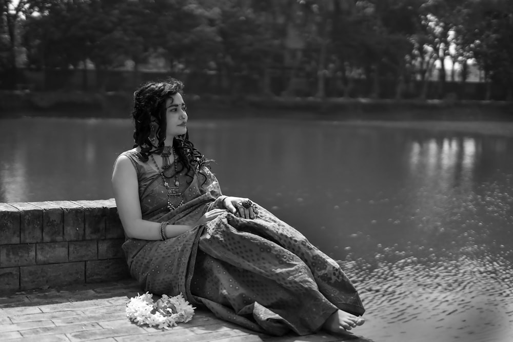 a woman sitting on a brick wall next to a lake