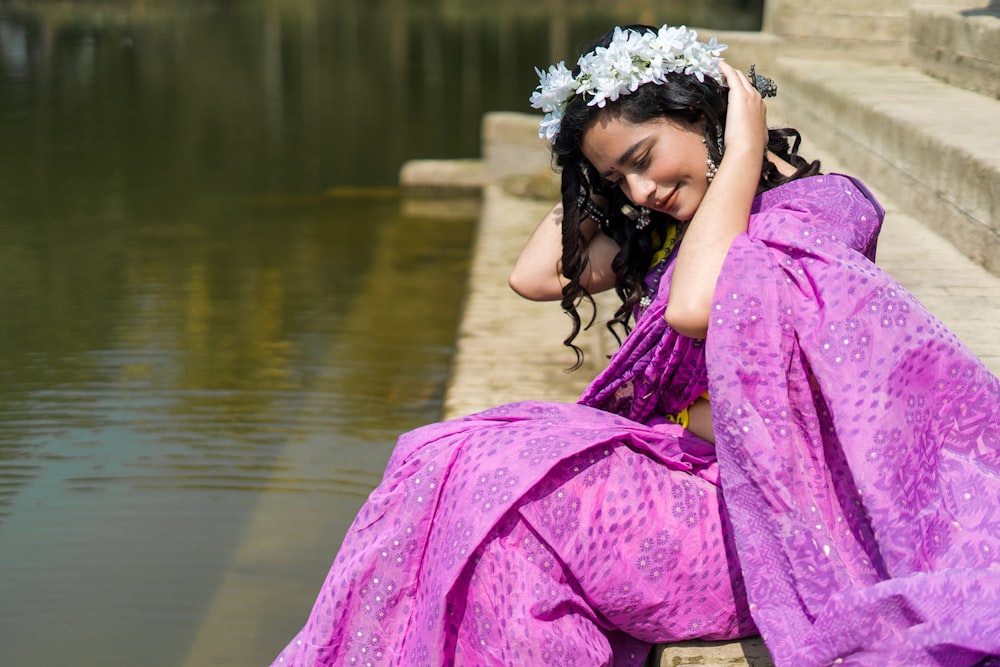 a woman in a purple dress sitting on a ledge next to a body of water