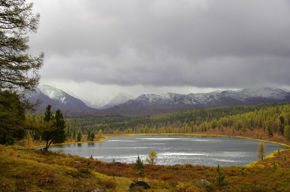 a lake surrounded by mountains under a cloudy sky