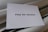 A piece of white paper with the words 'Pray for Ukraine' typed in a bold, black font is placed on a soft, light-colored fabric background.