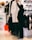 A person is selecting a white coat decorated with artistic drawings in a clothing store. The setting includes various apparel items such as hats, shoes, and jackets displayed on shelves and racks. The store has a modern ambiance with bright lighting.