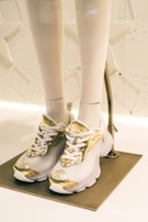 A stylish sneaker in white and gold placed on a modern display stand.