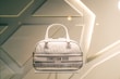A designer handbag is displayed against a stylish, geometric patterned background. The bag features a light color palette with elegant design elements and prominently showcases the brand 'Christian Dior' on the front.