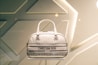 A designer handbag is displayed against a stylish, geometric patterned background. The bag features a light color palette with elegant design elements and prominently showcases the brand 'Christian Dior' on the front.