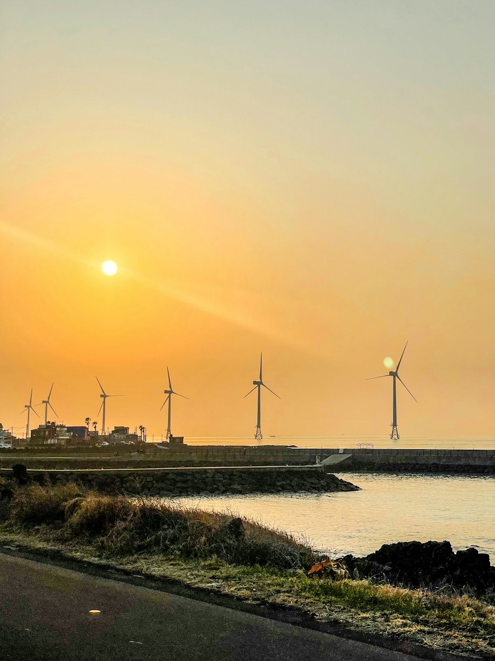 the sun is setting over a body of water with windmills in the background