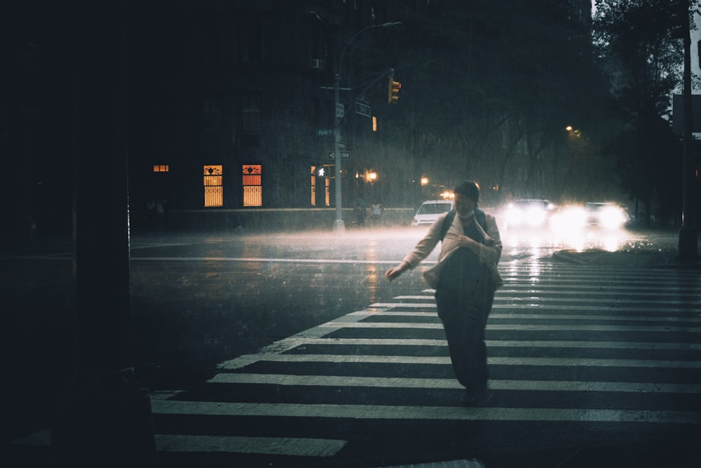 a woman walking across a street at night