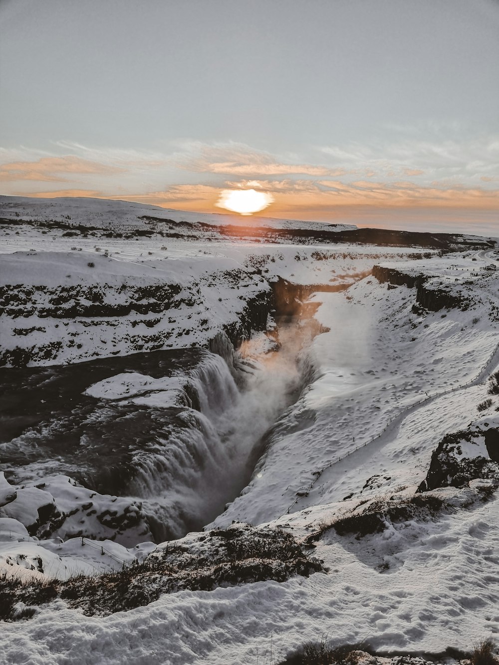 the sun is setting over a frozen waterfall