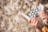 Hands holding allergy-related items including a nasal spray, blister pack of tablets, and a tissue against a backdrop of blurred flowering branches.