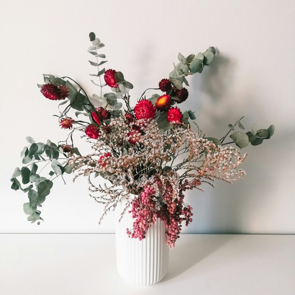 a white vase filled with red flowers and greenery
