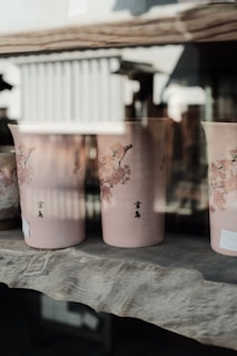 A close-up of elegant ceramic vases in soft pink and cream hues on a wooden shelf.