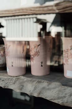 A close-up of elegant ceramic vases in soft pink and cream hues on a wooden shelf.