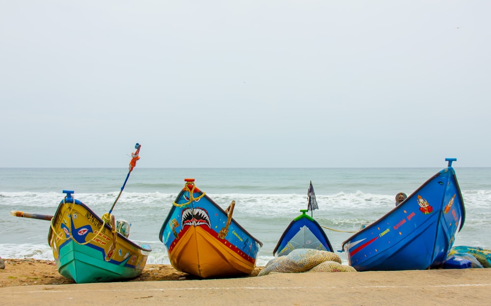 a group of three boats sitting on top of a sandy beach