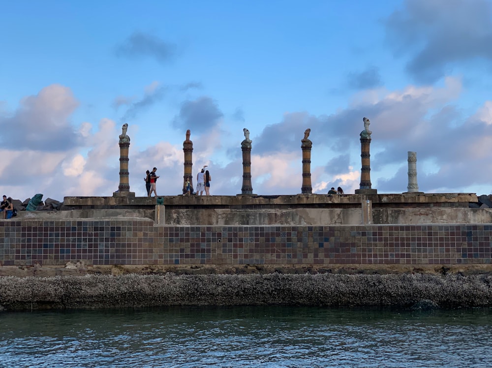 a group of people standing on top of a wall next to a body of water