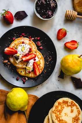 Close-up of golden pancake skewers drizzled with honey and sprinkled with crushed nuts on a cream-colored plate.