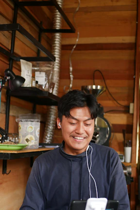 A young woman smiling while using sleek wireless earbuds in a cozy cafe.