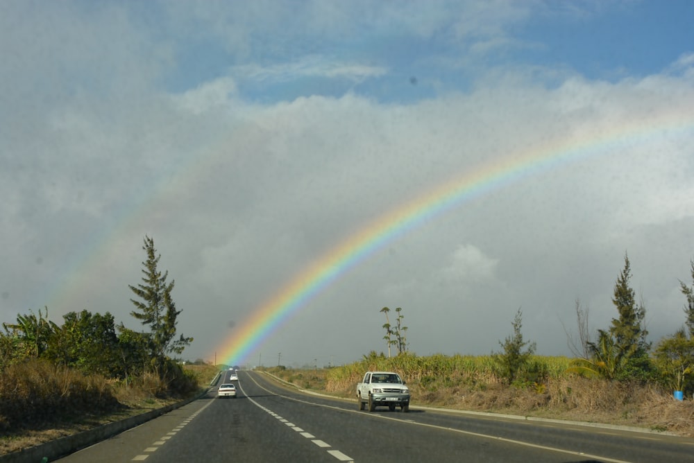 a car driving down a road with a rainbow in the sky