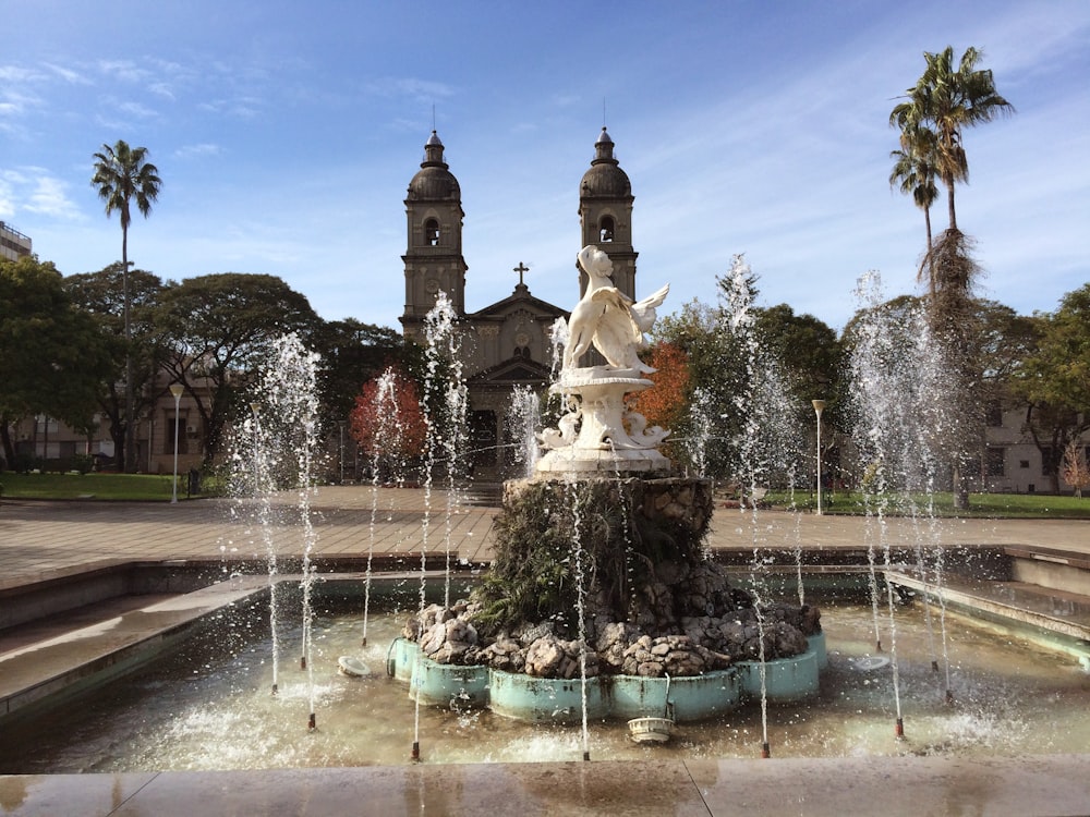 uma fonte em frente a um edifício com uma torre do relógio ao fundo