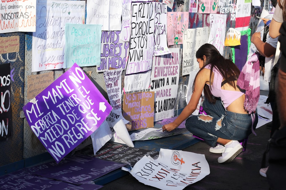 a woman kneeling down next to a wall covered in signs